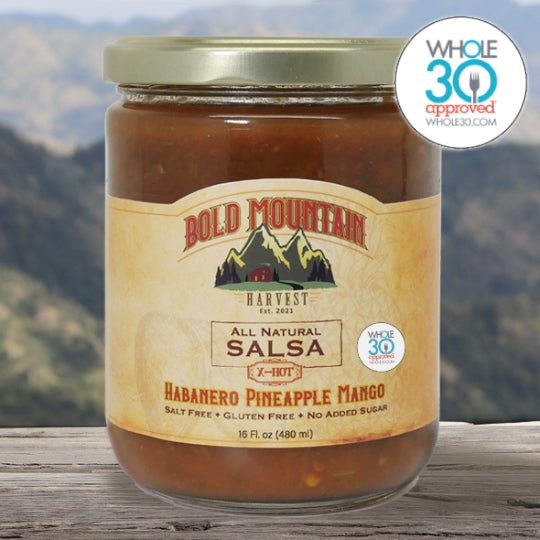 The Whole 30 Approved logo is shown with a 16-ounce jar of Bold Mountain Harvest Habanero Pineapple Mango Salsa. The product is marked X-hot and is in front of a mountain view.