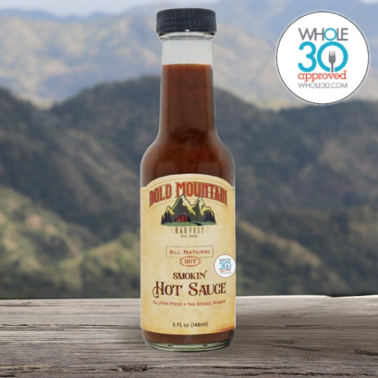 The Whole 30 approved logo with a 5 ounce jar of Bold Mountain Harvest Smokin’ Hot Sauce in front of a mountain view.